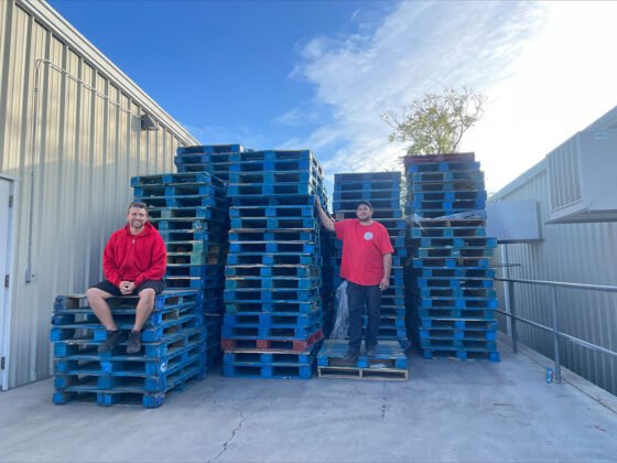 Manzanita Outreach Executive Director Ben Burke and Warehouse & Distribution Manager Jimmie Treakle pose with over 200 excess pallets collected from Manzanita operations. Manzanita volunteers and staff upcycle pallets and cardboard to create shade structures, raised garden beds, and composting bins.