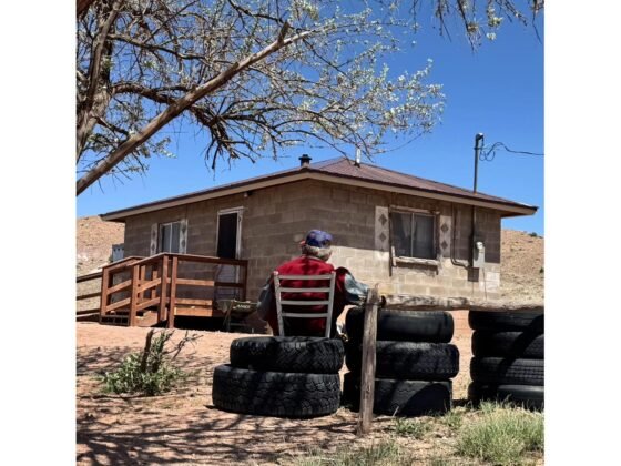 An elderly Navajo man, Charley Billy, smiles outside his home, which recently received renovations through Yee Ha'ólníi Doo's 'Owner-Occupied Housing Health and Safety' initiative. The improvements include a newly built access ramp and a new roof. Previously, the homeowner struggled with unsafe steps and lacked a handrail, leading to a fall last year, and relied on neighbor assistance for roof repairs. The initiative is funded by the Arizona Department of Housing, providing critical support to vulnerable households in Northern Arizona.
